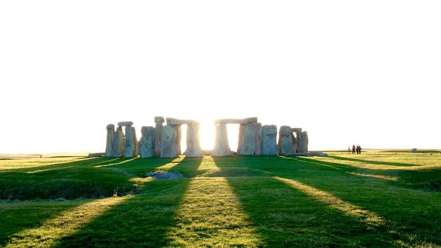 Tourists at Stonehenge under bright sun casting long shadows