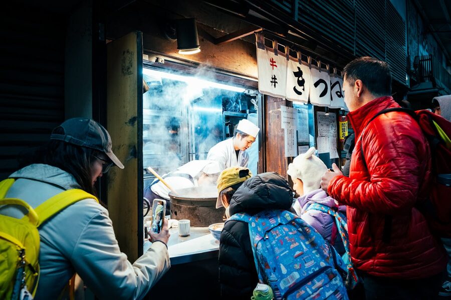 A busy street food stall in Tokyo at night with customers gathering around steaming food displays