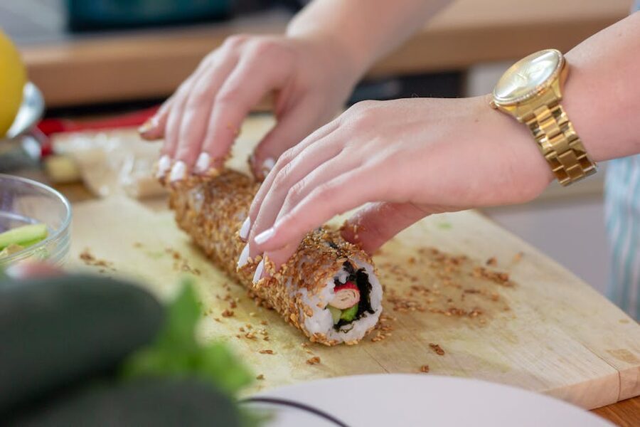 Hands rolling sesame-coated sushi on wooden board