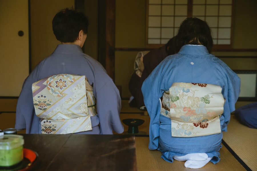 Back view of anonymous people in authentic robes sitting on tatami