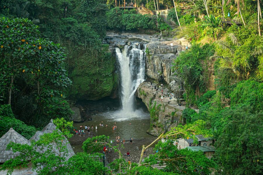 travellers at the base pool of Tegenungan waterfall with spray in the air