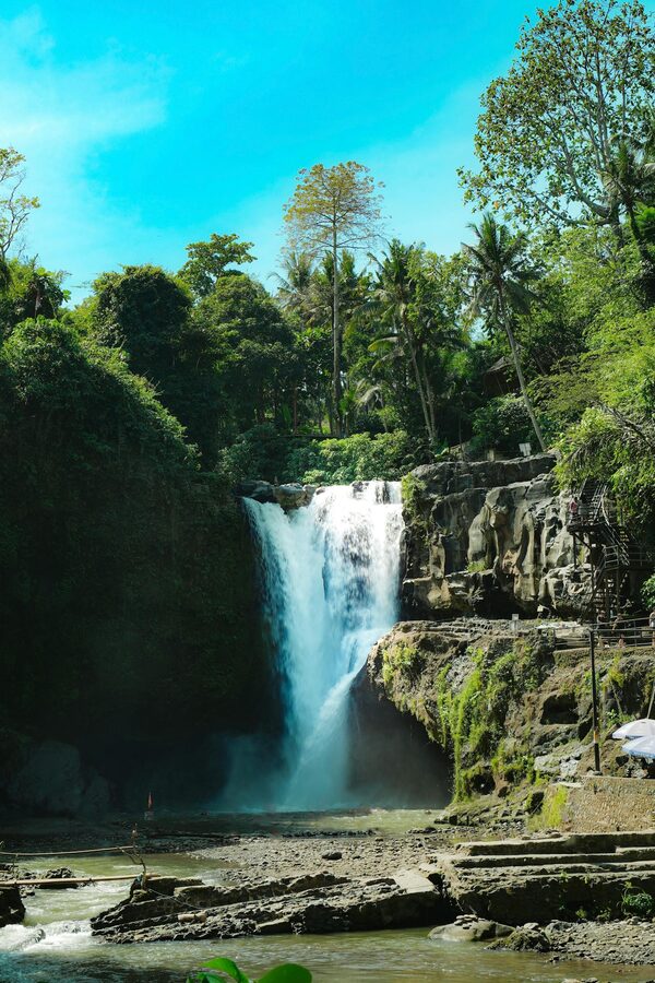 Wide view of Tegenungan waterfall in Bali with mist rising from the base and green jungle around