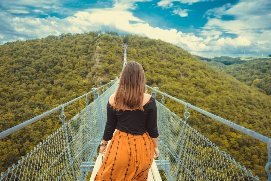 Woman walking on a canopy bridge suspended above forest floor with hills in background