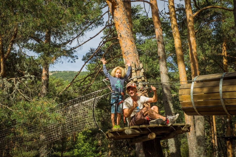 Father and young child riding a zipline together through forest
