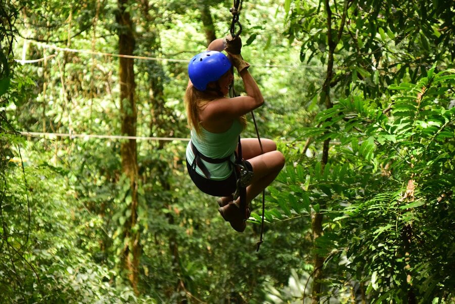 Woman wearing safety gear ziplining through lush green forest canopy