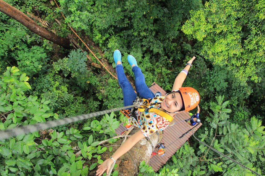 Woman wearing safety helmet on a zipline through green forest in Phuket Thailand