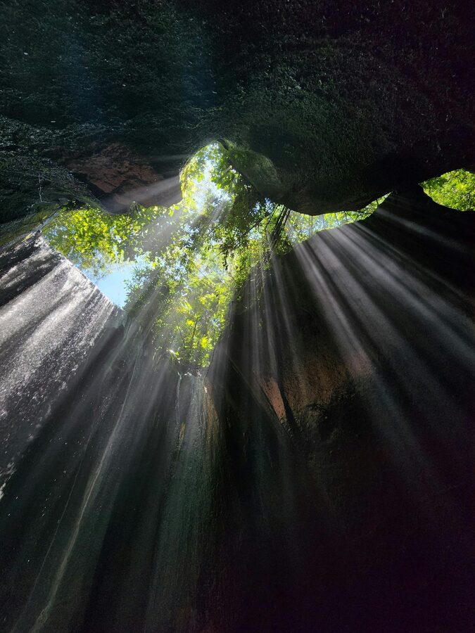 Tibumana waterfall veil dropping into a quiet jungle pool with travellers in the water