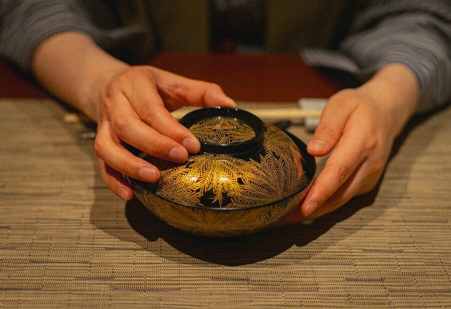 Hands holding a traditional Japanese lacquerware bowl at a dinner table