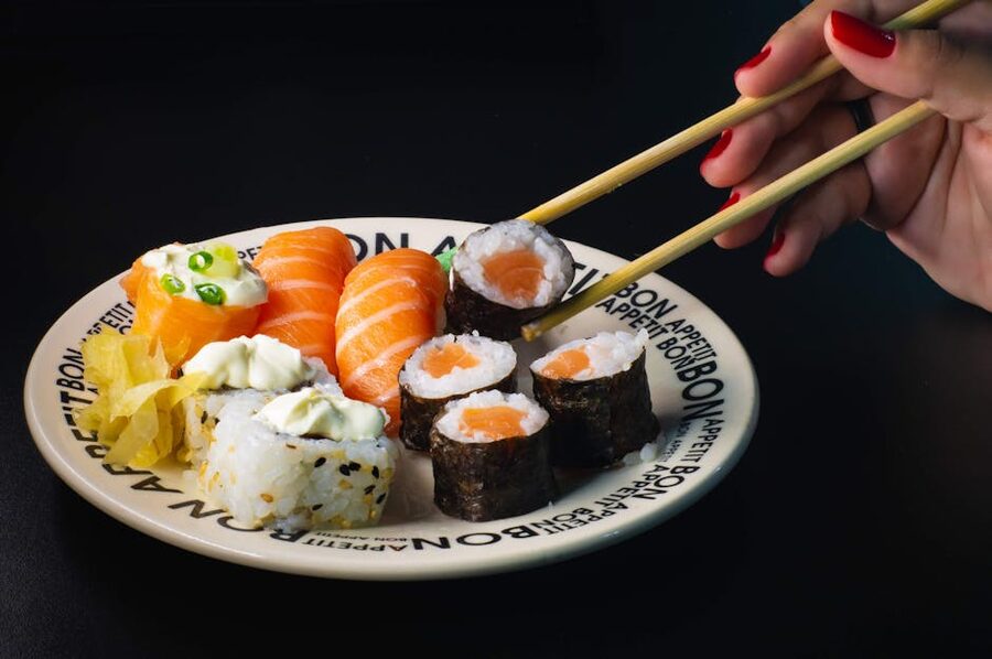 Hand using chopsticks to lift a maki roll from a platter