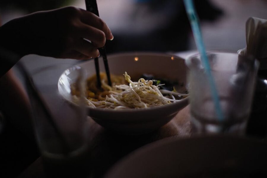 Hand using chopsticks to lift Asian noodles from a bowl