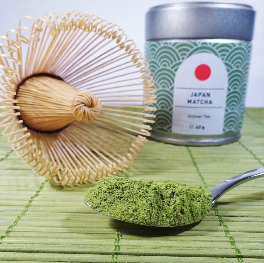 Matcha green tea powder beside a bamboo chasen whisk