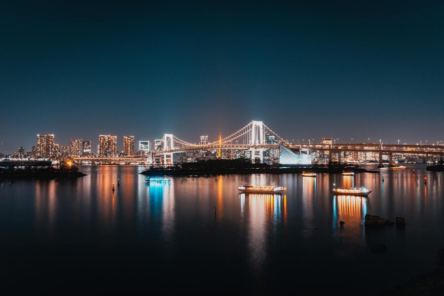 Night panorama of Rainbow Bridge and Tokyo skyline with reflections on the bay
