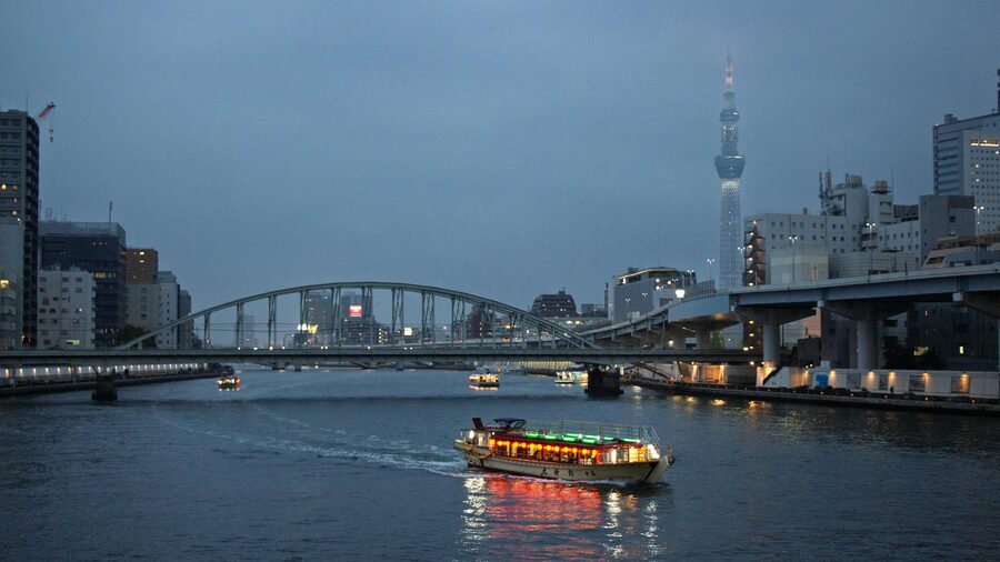 Tokyo Skytree towering above an illuminated cruise boat on the river at night