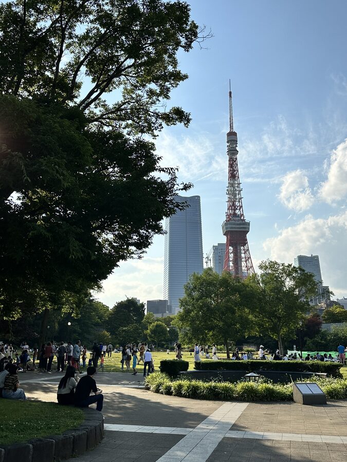 Tokyo Tower rising above lush green trees as seen from Shiba Park
