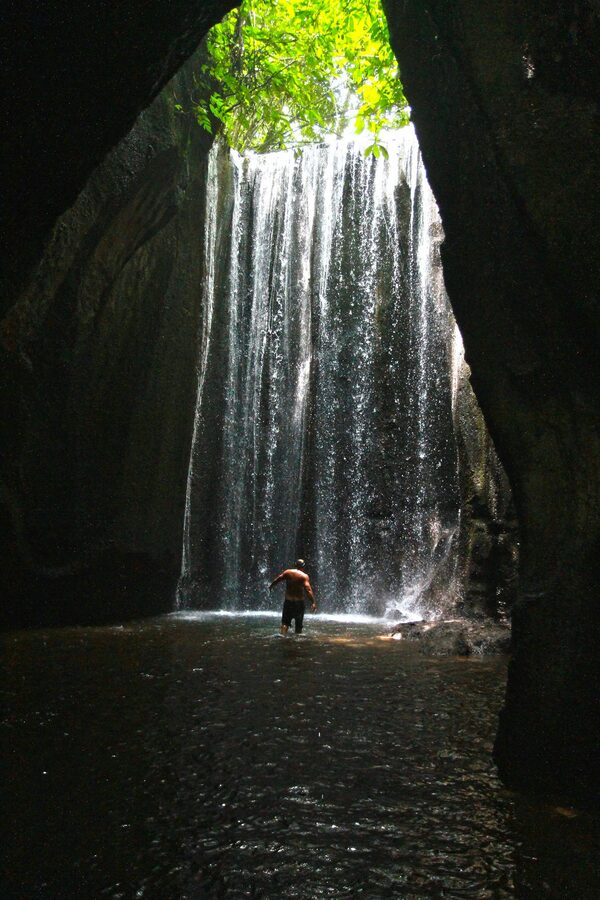 travellers wading through a shallow stream toward the entrance of Tukad Cepung cave waterfall