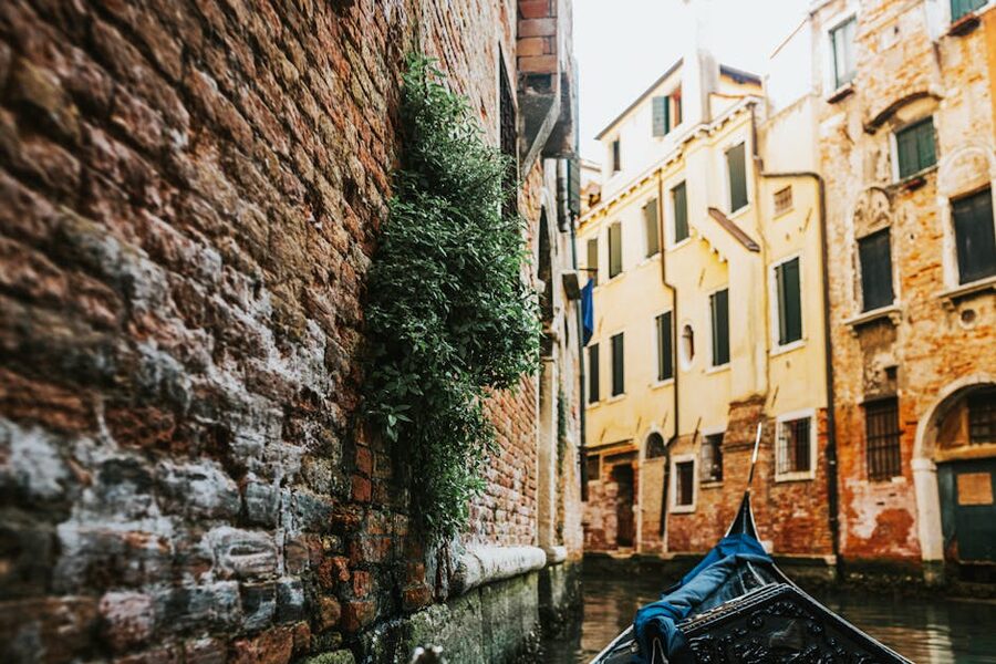 Black gondola gliding past brick wall on quiet Venice side canal