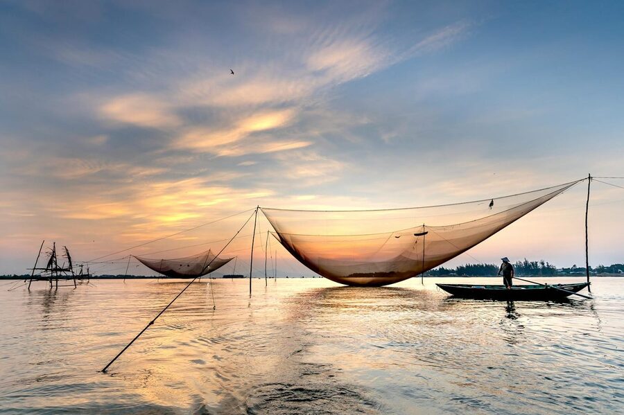 Fisher on river with traditional lift net at sunset in Vietnam