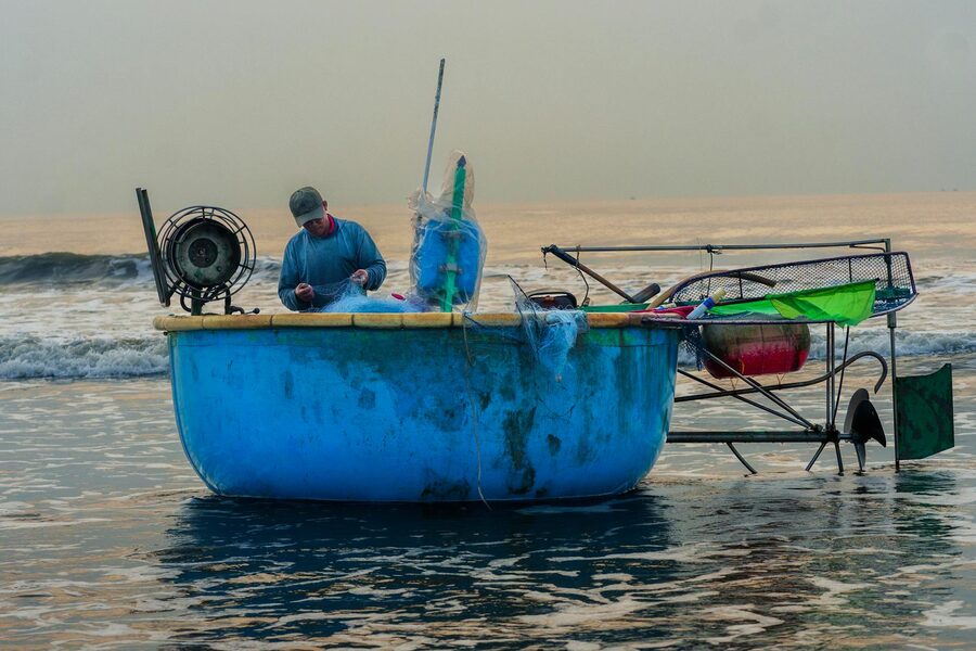 Vietnamese fisherman preparing nets in a traditional blue basket boat