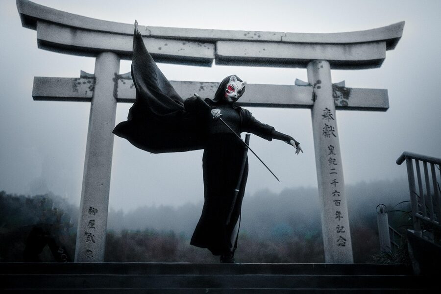 Warrior in cloak with sword standing by a torii traditional Japanese gate
