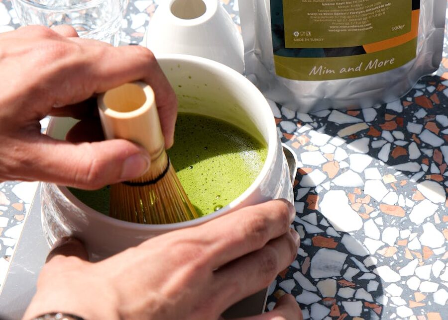 Whisking matcha tea with bamboo whisk in white bowl