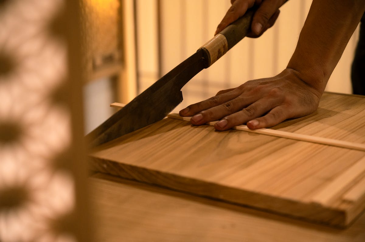 Close-up of a hand using a traditional Japanese saw to make a precise cut in wood