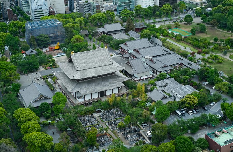 Aerial view of historic Zojoji Temple surrounded by greenery with Tokyo Tower rising behind it