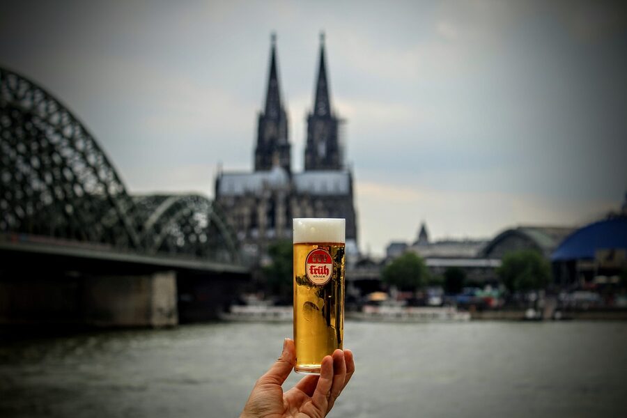 Kolsch beer raised to Cologne Cathedral and Hohenzollern Bridge at sunset