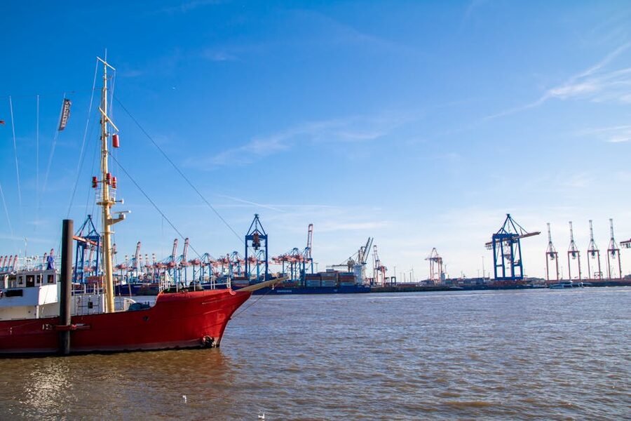 Red sailboat in front of Hamburg harbor cranes