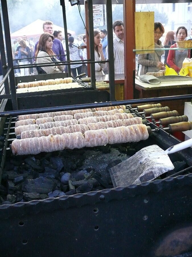 Trdelnik dough cooking on rotating sticks over coals at a Prague stand