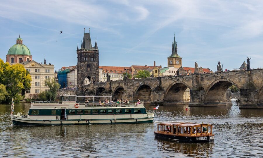 Daytime cruise boat passing through the Charles Bridge arches on the Vltava