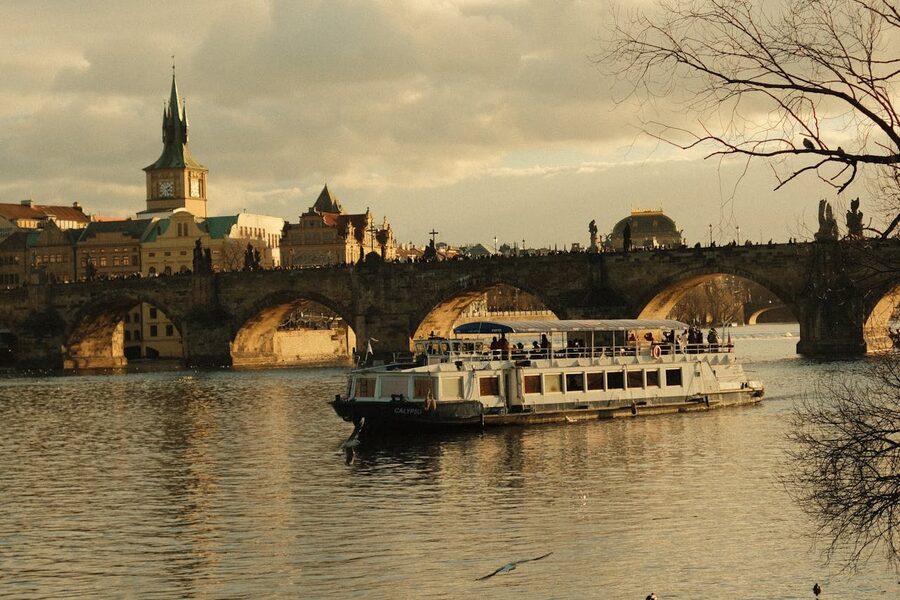 Sightseeing boat passing under Charles Bridge on the Vltava at golden hour